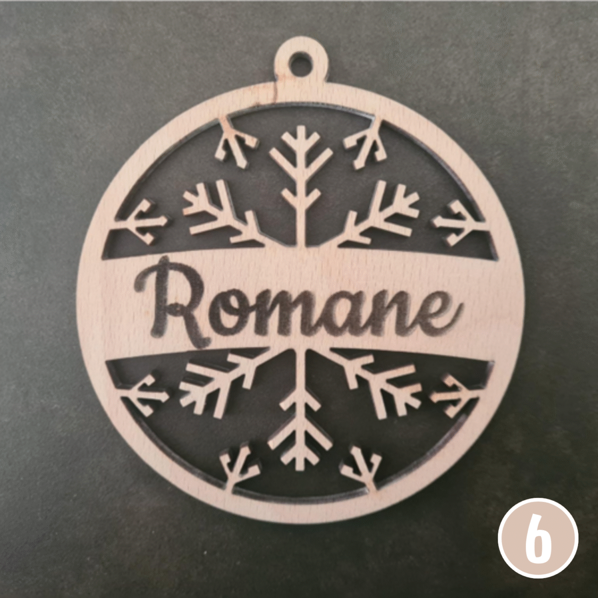 Décoration de Noël ronde en bois présentant le prénom "Romane" entouré de motifs ajourés complexes de branches et feuilles, avec trou de suspension en haut
