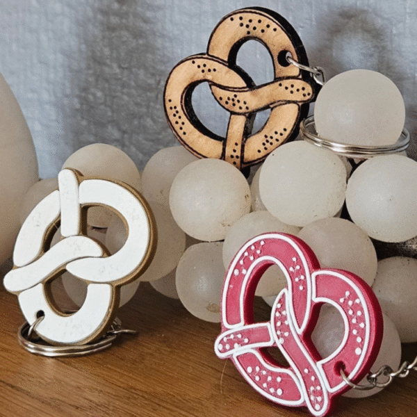 Porte-clés bretzel 3D artisanaux en plusieurs couleurs disposés sur une table en bois avec un raisin blanc en arrière-plan - fabrication française par impression 3D
