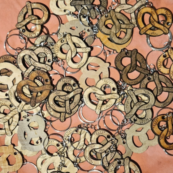 Collection de porte-clés bretzel en bois naturel avec anneaux métalliques sur fond rose saumon - fabrication artisanale française par découpe laser - nuances de bois variées