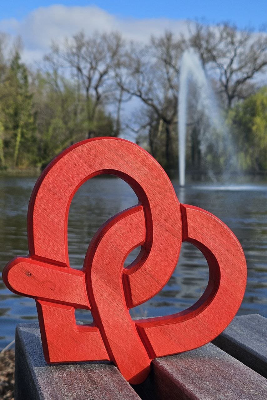 Dessous de plat Bretzel Coeur en bois rouge en forme de cœur posée sur un banc en bois près d'un bassin avec fontaine dans un parc